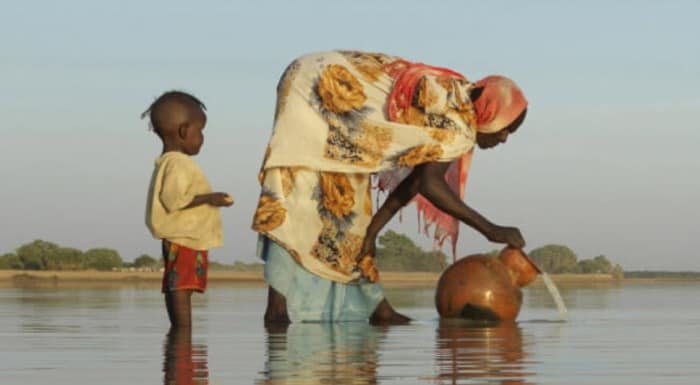 Women drawing water from a river with her child